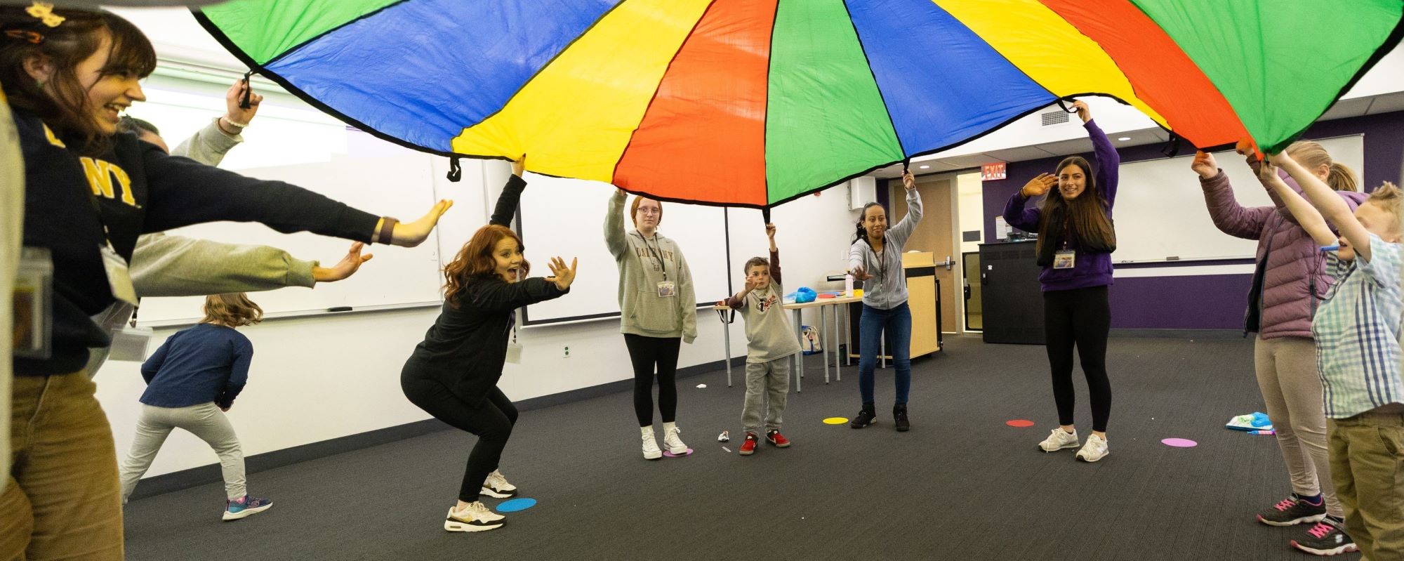 UAlbany students and kids from the Friday Knights program playing with a parachute.