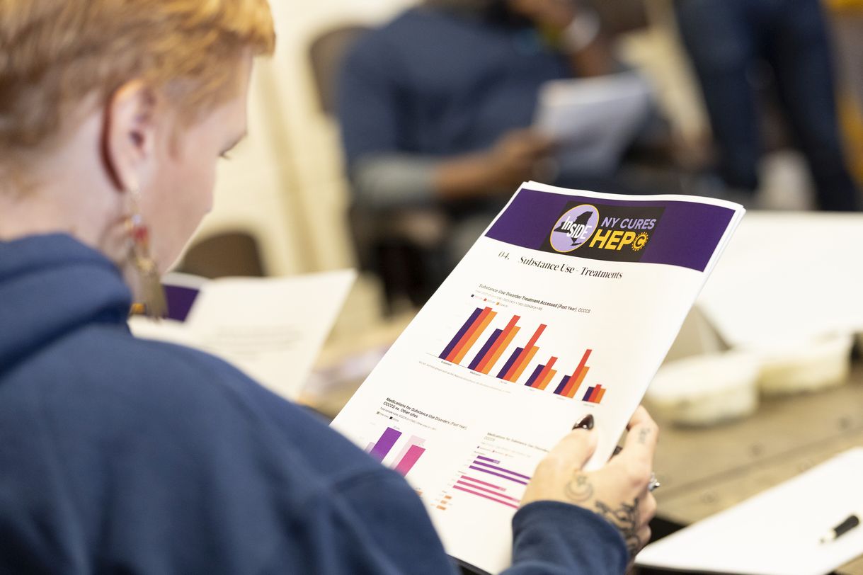 A person with short red hair wearing a navy hoodie holds a booklet with colorful barcharts 
