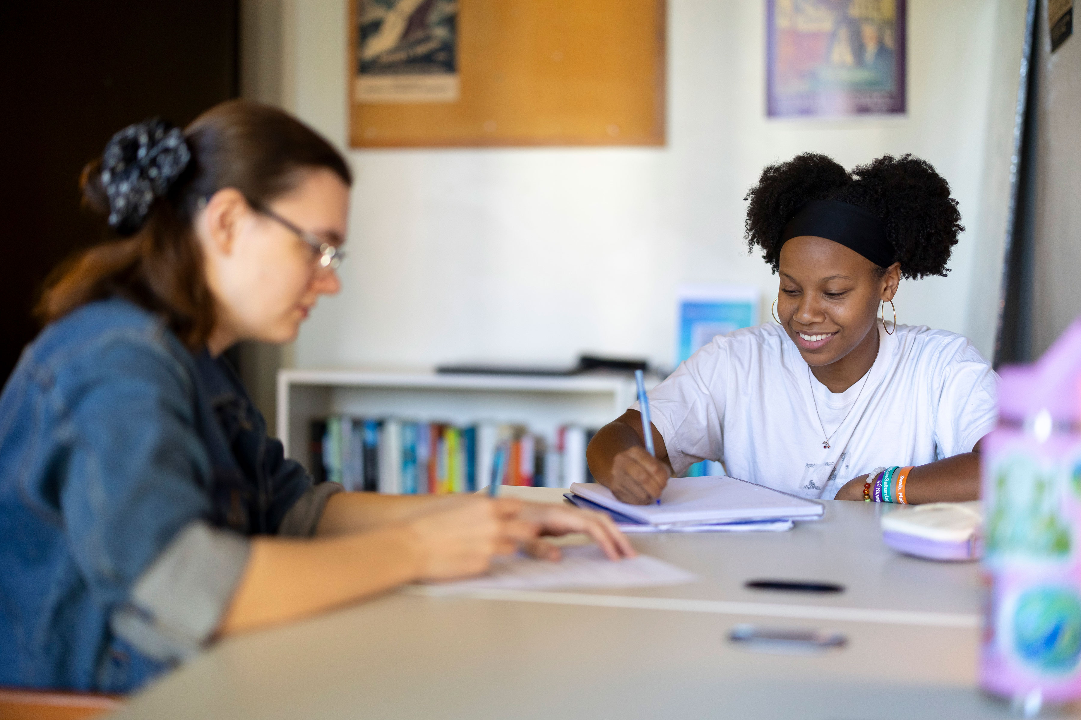 An image of two students sitting at a table and both are writing on a piece of paper.