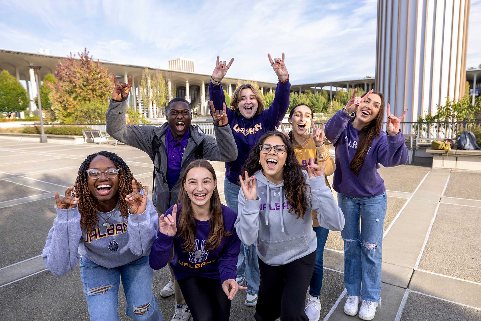 Seven students outside on the podium making Damien signs with their hands.