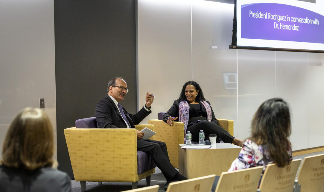 Two people engaged in lively conversation sit in yellow and purple armchairs at the front of a conference room.