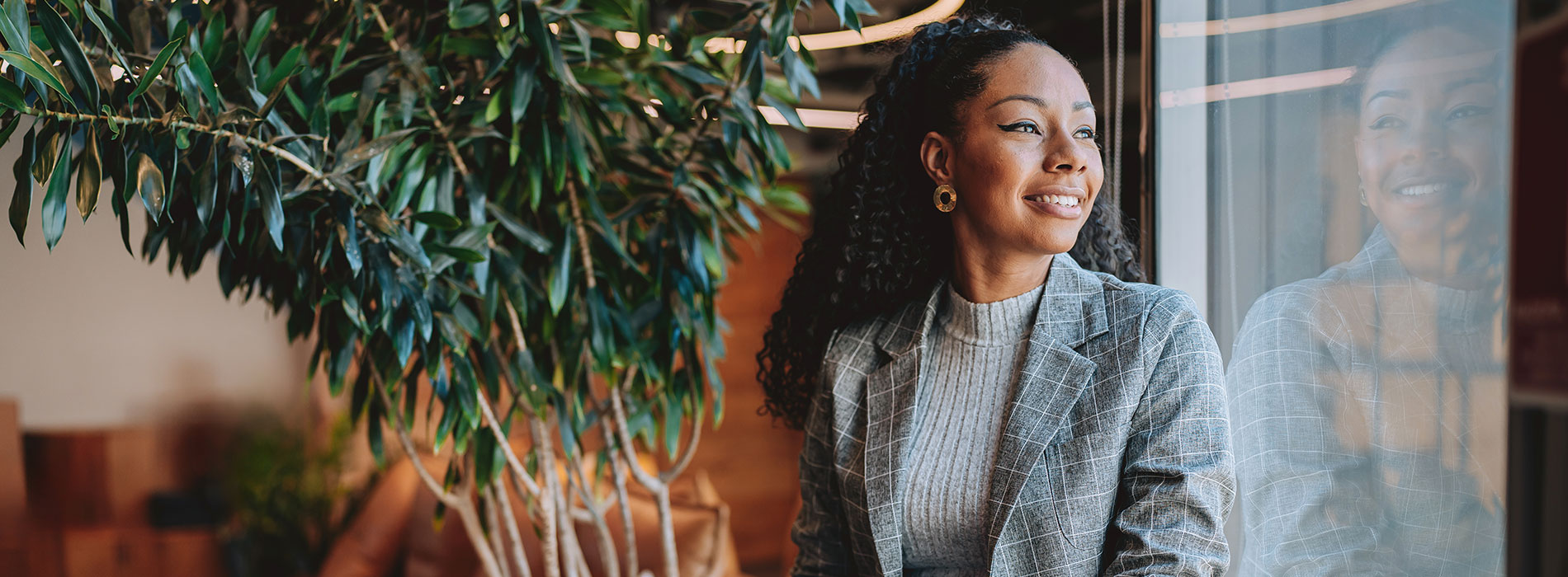 A smiling professional in communications or marketing sitting by a window holding a laptop.