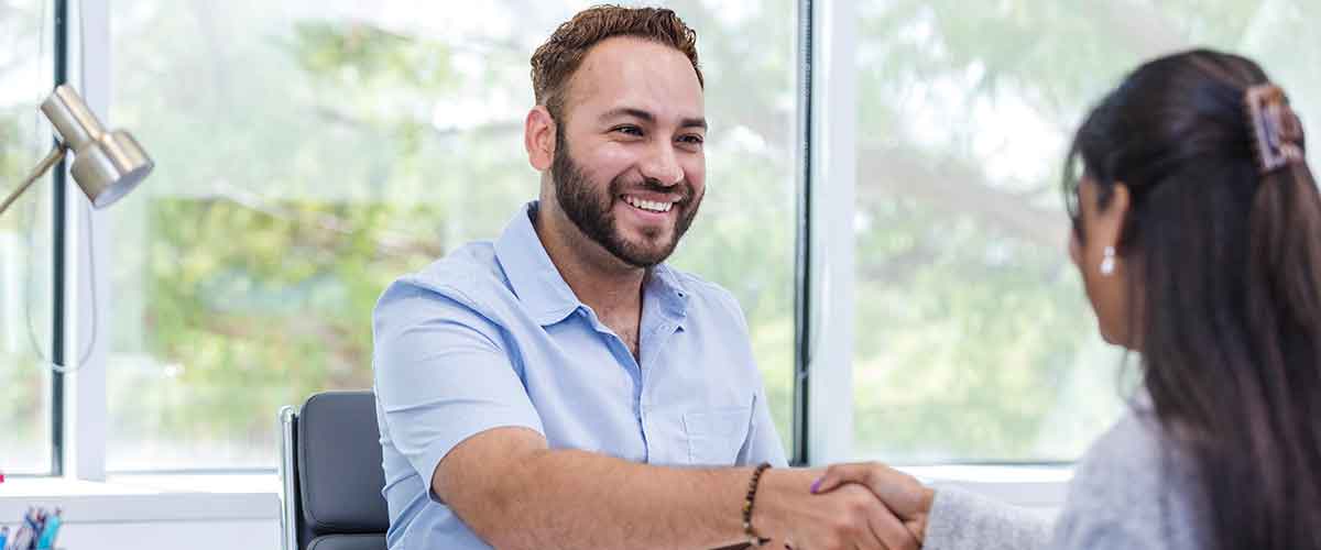 A career counselor seated at a desk shakes hands with a client.