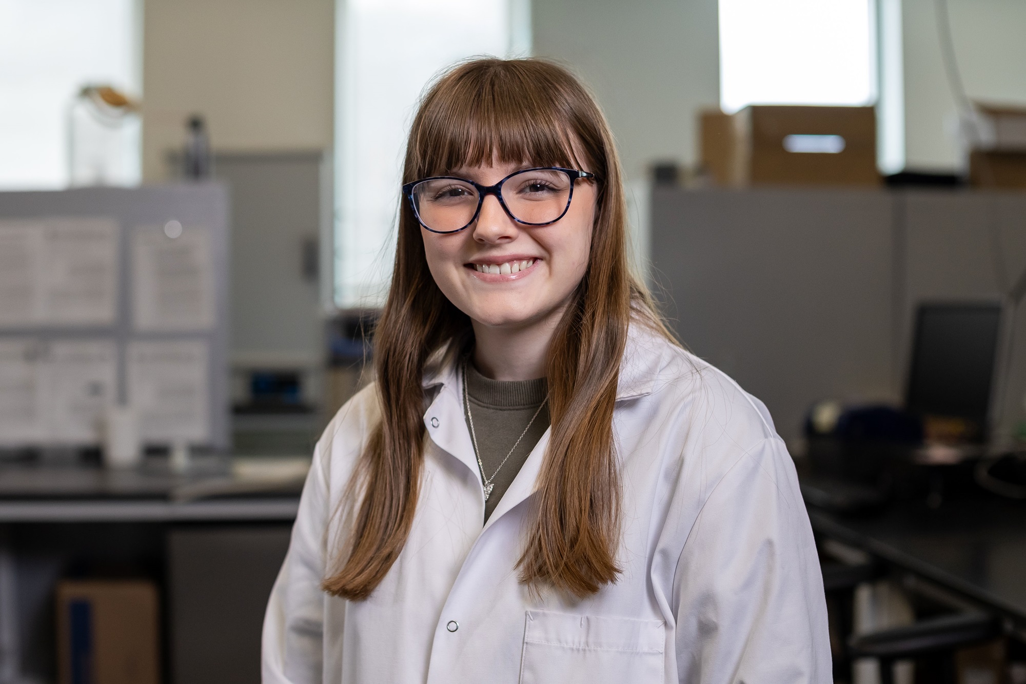 UAlbany undergraduate researcher Katelyn Jacques smiles while wearing a lab coat inside UAlbany's Paleoclimate Lab.