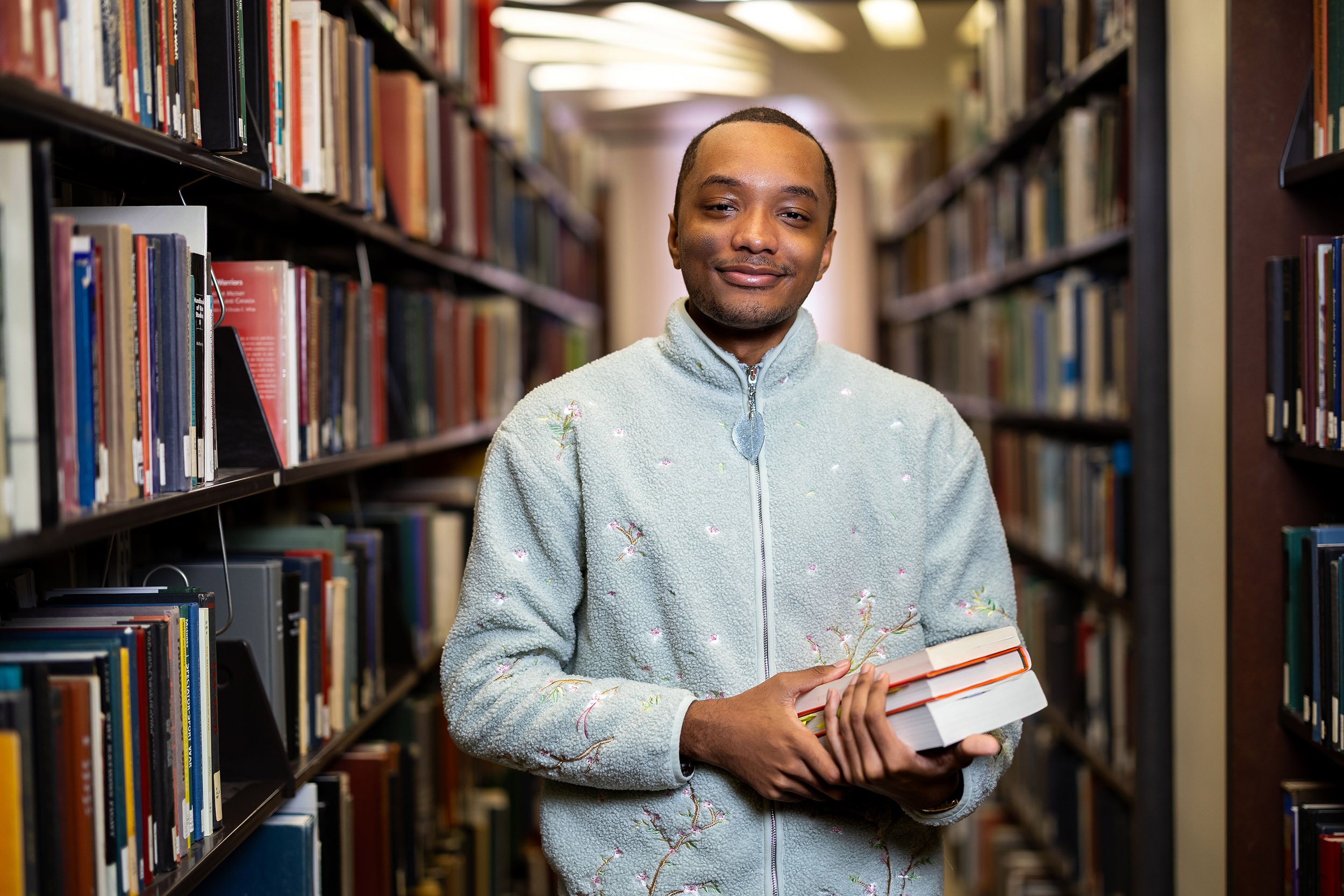 UAlbany student Maurice Burbridge inside the UAlbany library as he stands in front of stacks of books.
