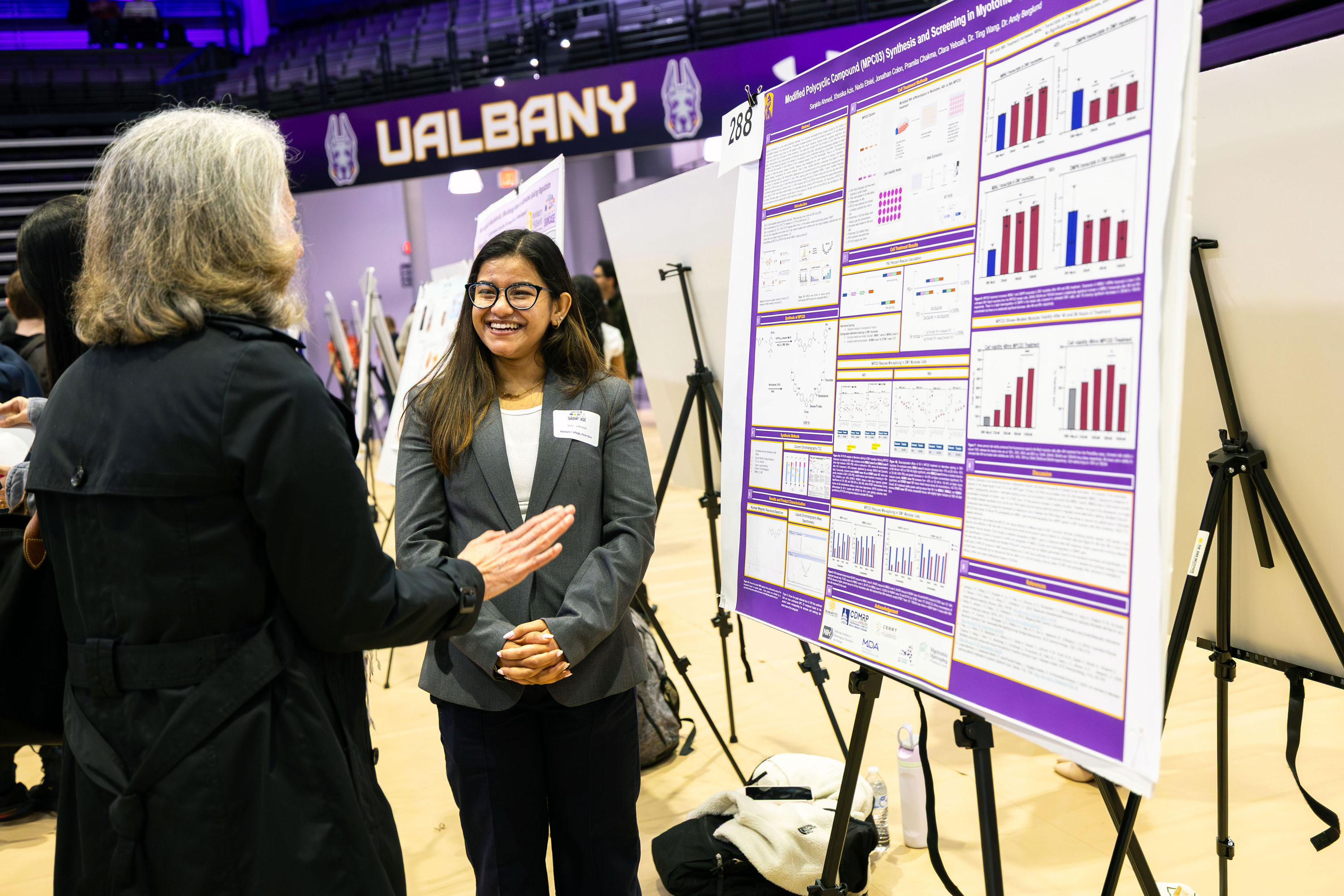 A student presenter smiles while speaking with a Showcase attendee admiring her research poster.