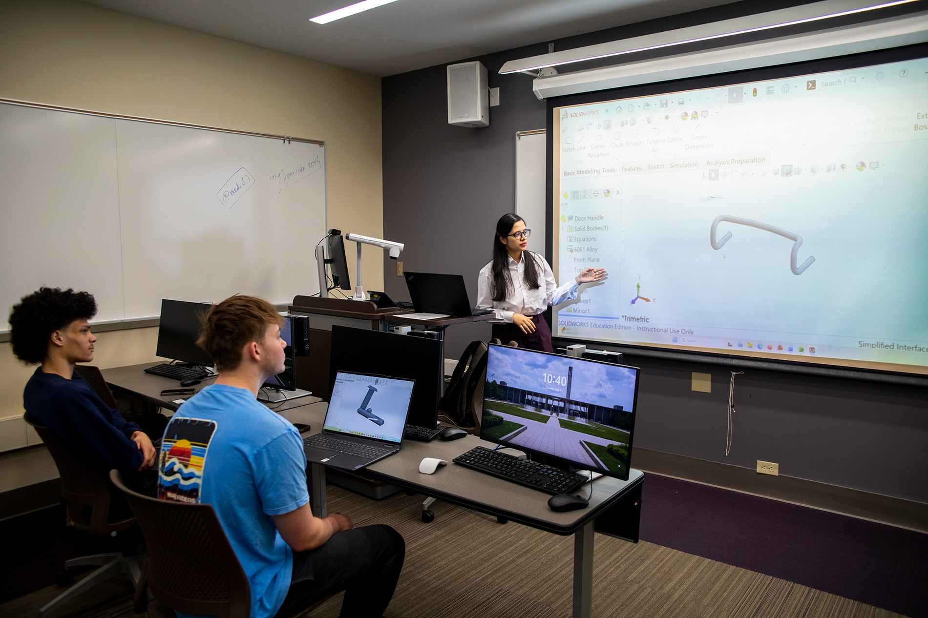 An instructor teaches a class of students in the MME program.