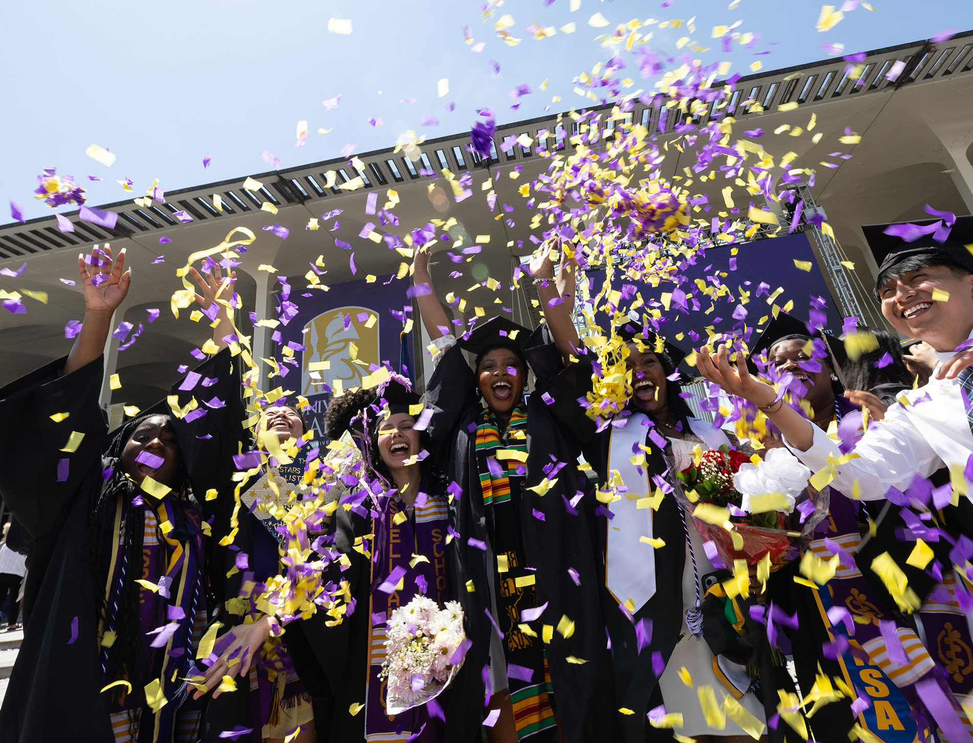 A group of students in full regalia celebrating at commencement by throwing confetti in the air.