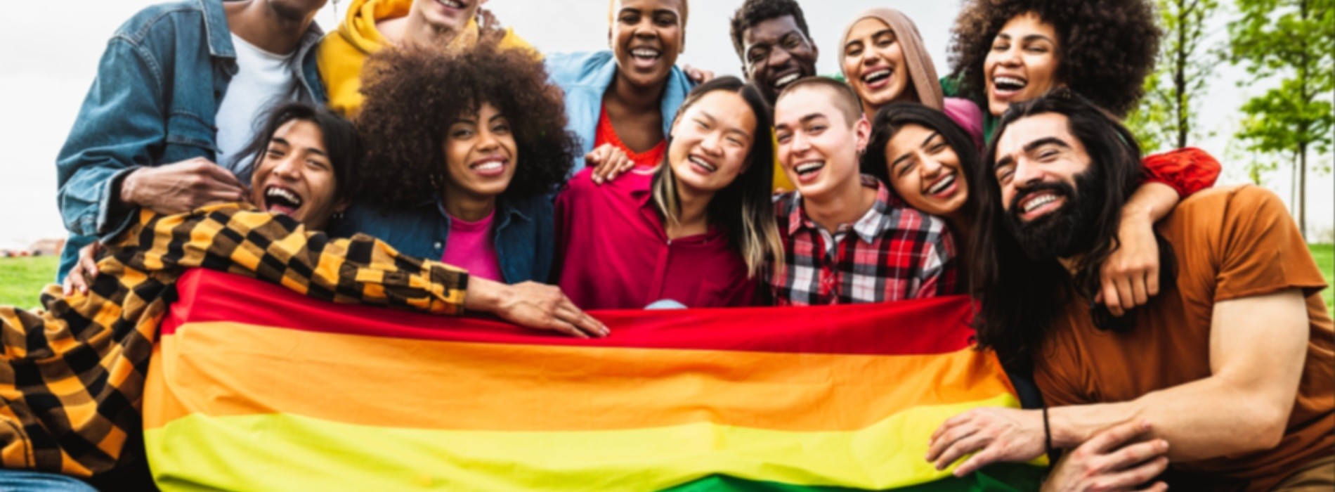A group of smiling students pose with a rainbow flag.