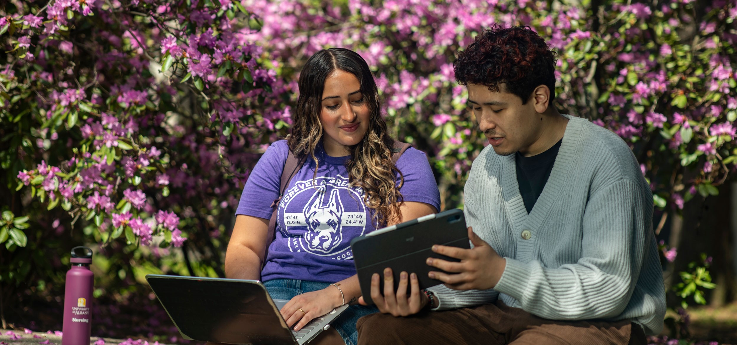 Two students sitting outside and looking at a tablet screen.