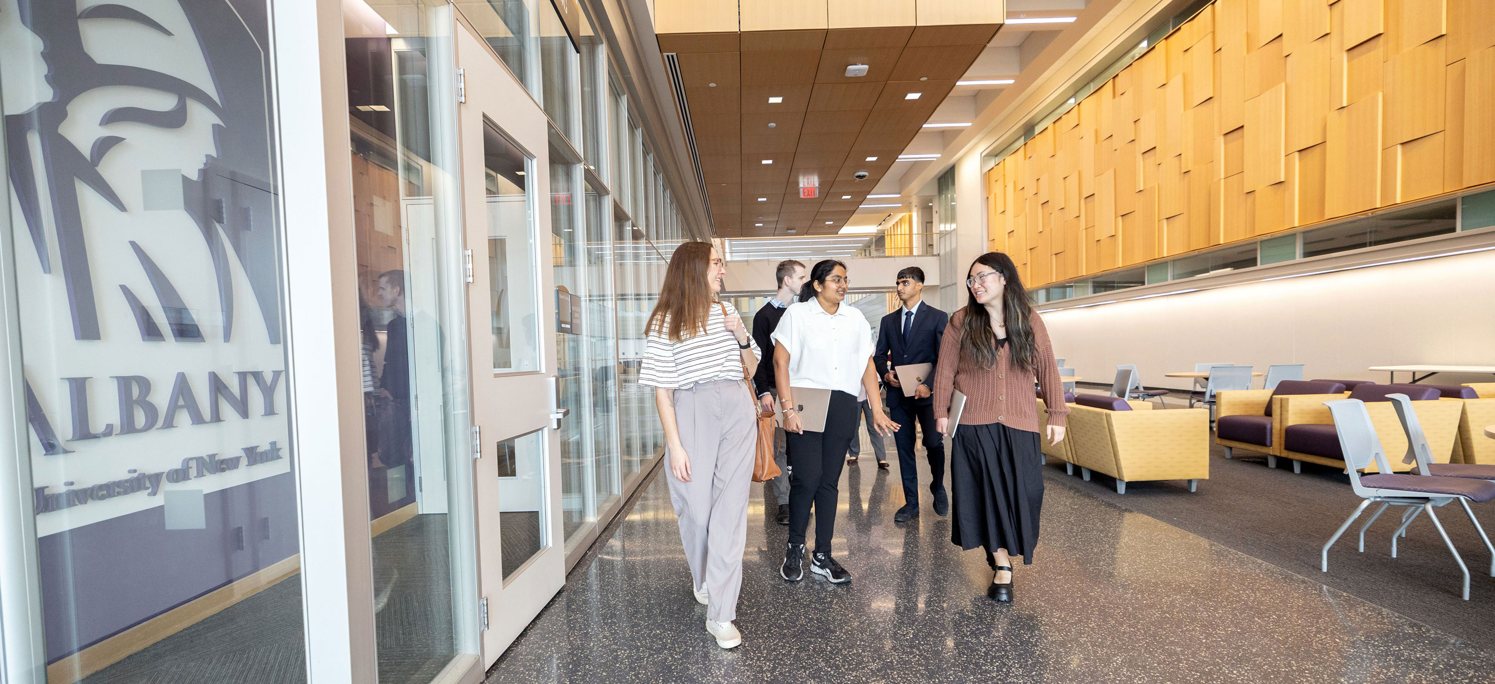 Five graduate students chat as they walk down a hallway.