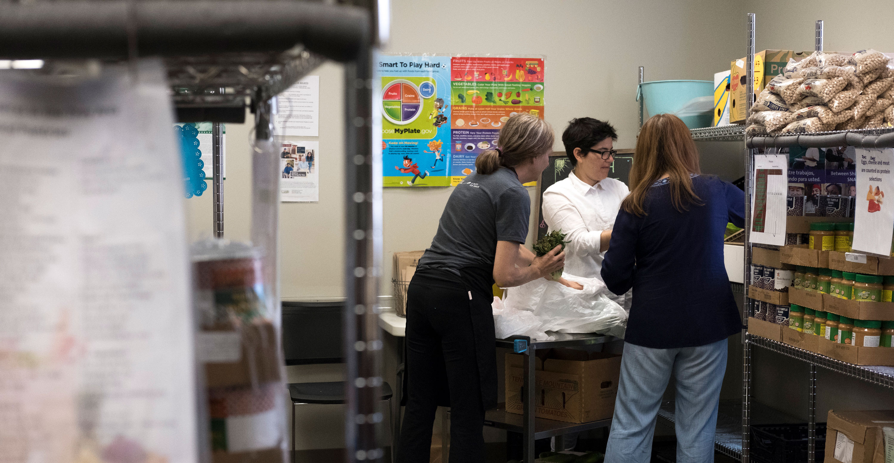 Three adults work inside a food pantry stocking shelves.