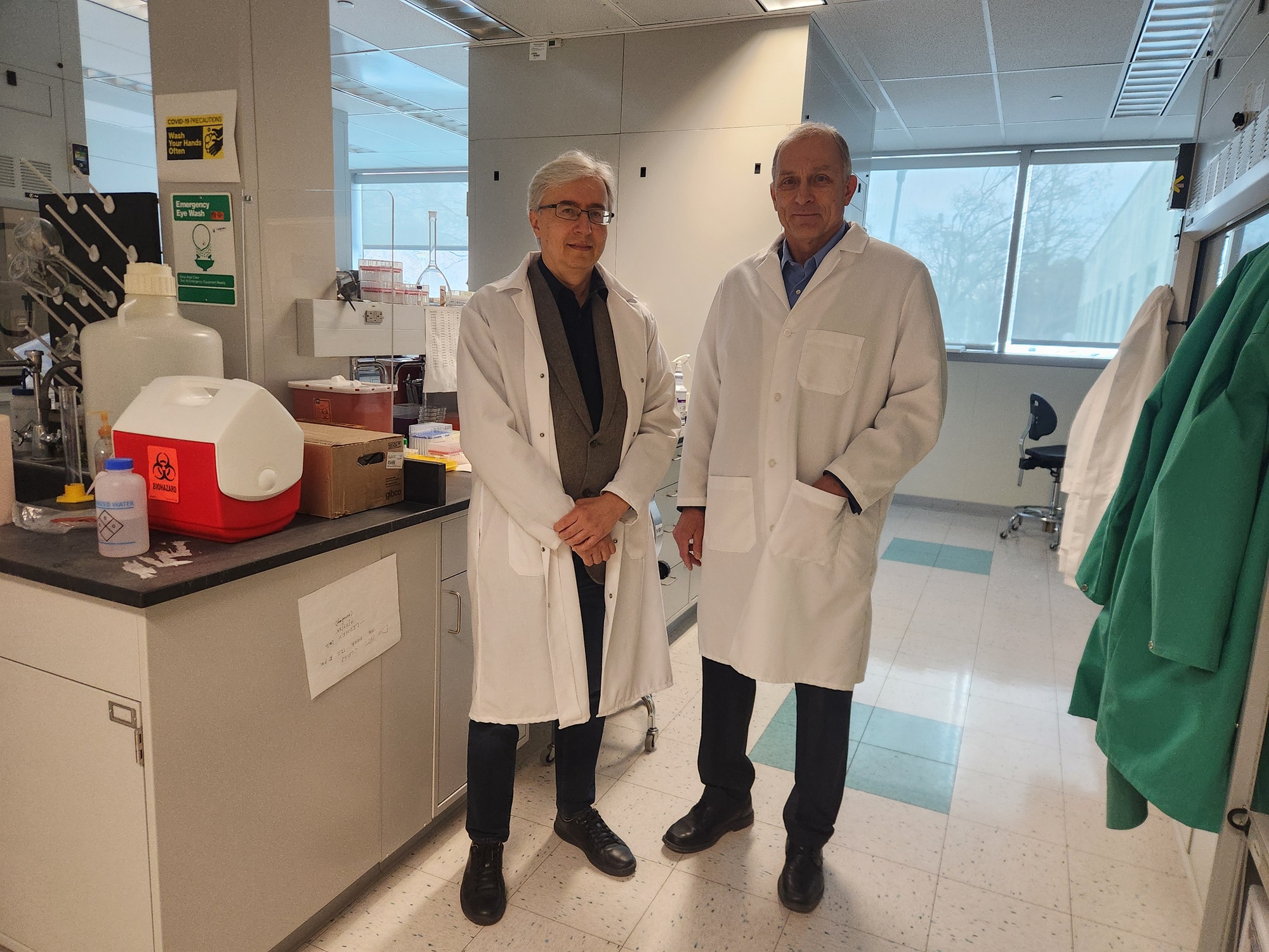 Alexander Shekhtman and Igor Lednev stand in white lab coats inside a chemistry lab.