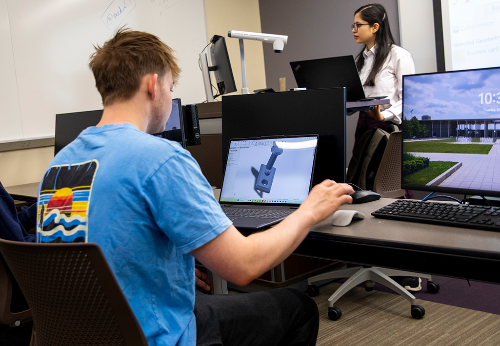 A student listens to a professor in class in the MME program while they use a computer.