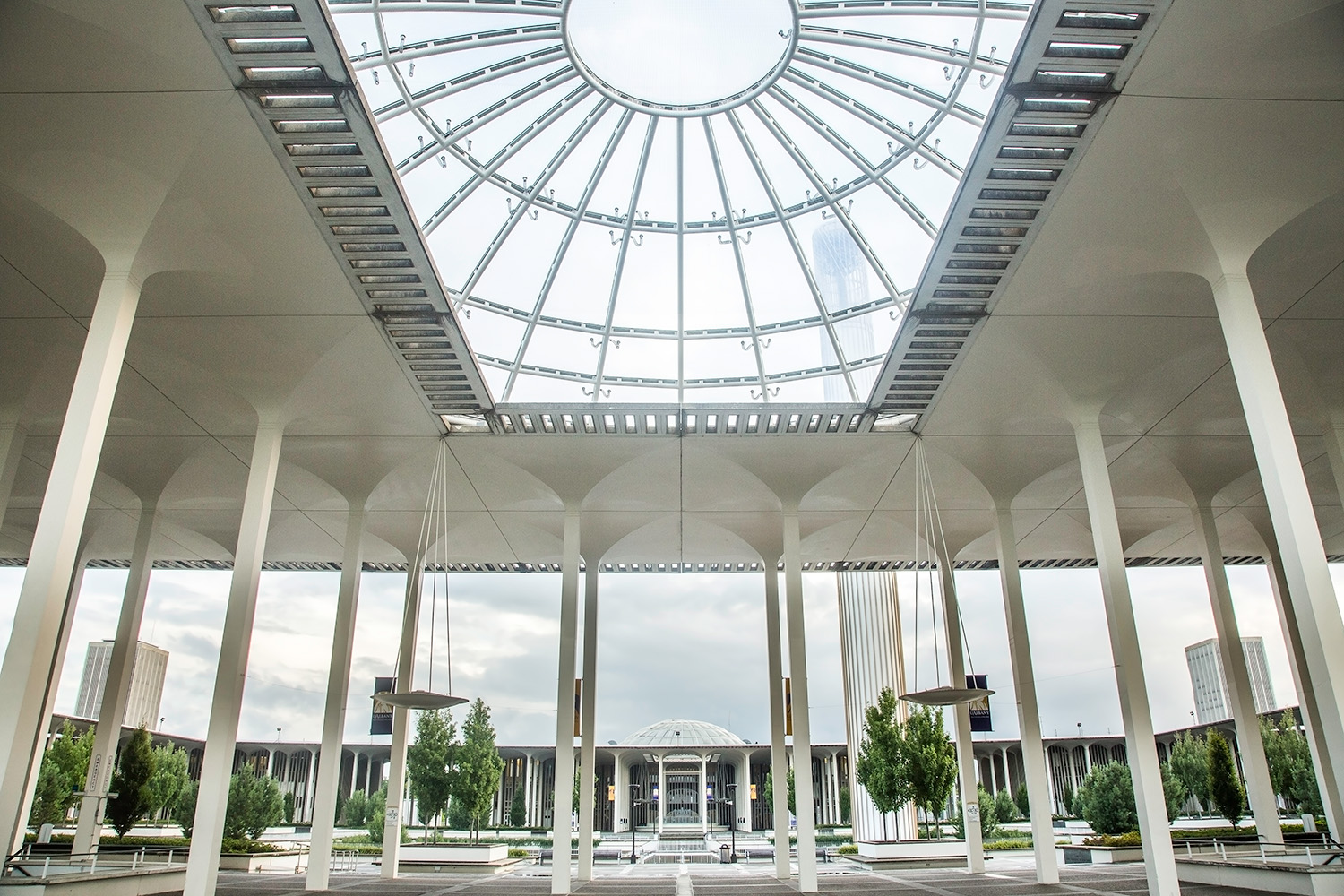 UAlbany's main campus shot with tall columns holding up a windowed roofing structure. The campus fountain can be seen in the background. It is a cloudy but beautiful day on campus.