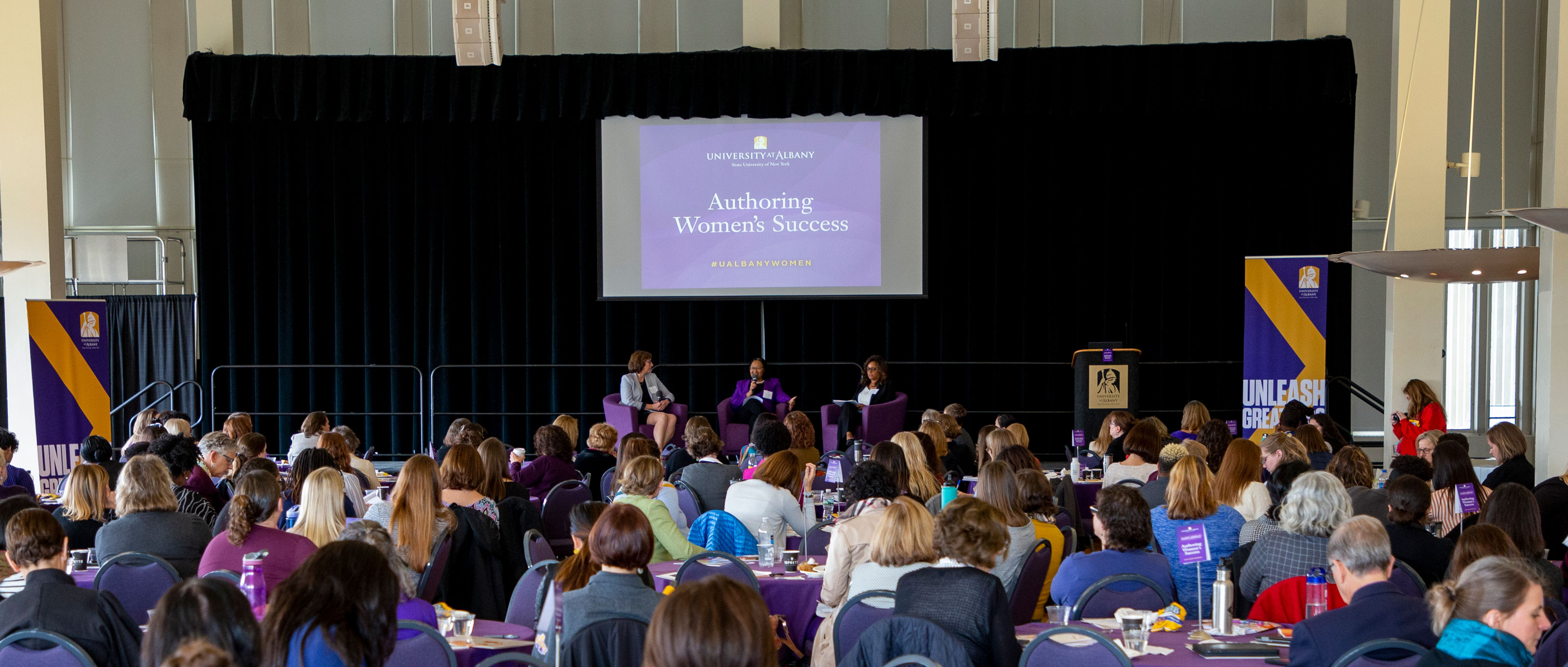An audience seated at round tables listens as a panel of three women speak at the Authoring Women’s Success event.