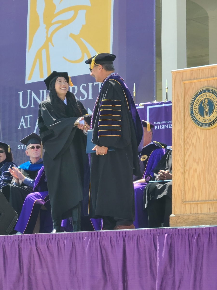 Nora Lum shakes the hand of UAlbany President Havidán Rodríguez as she receives her honorary doctorate at UAlbany's commencement ceremony.