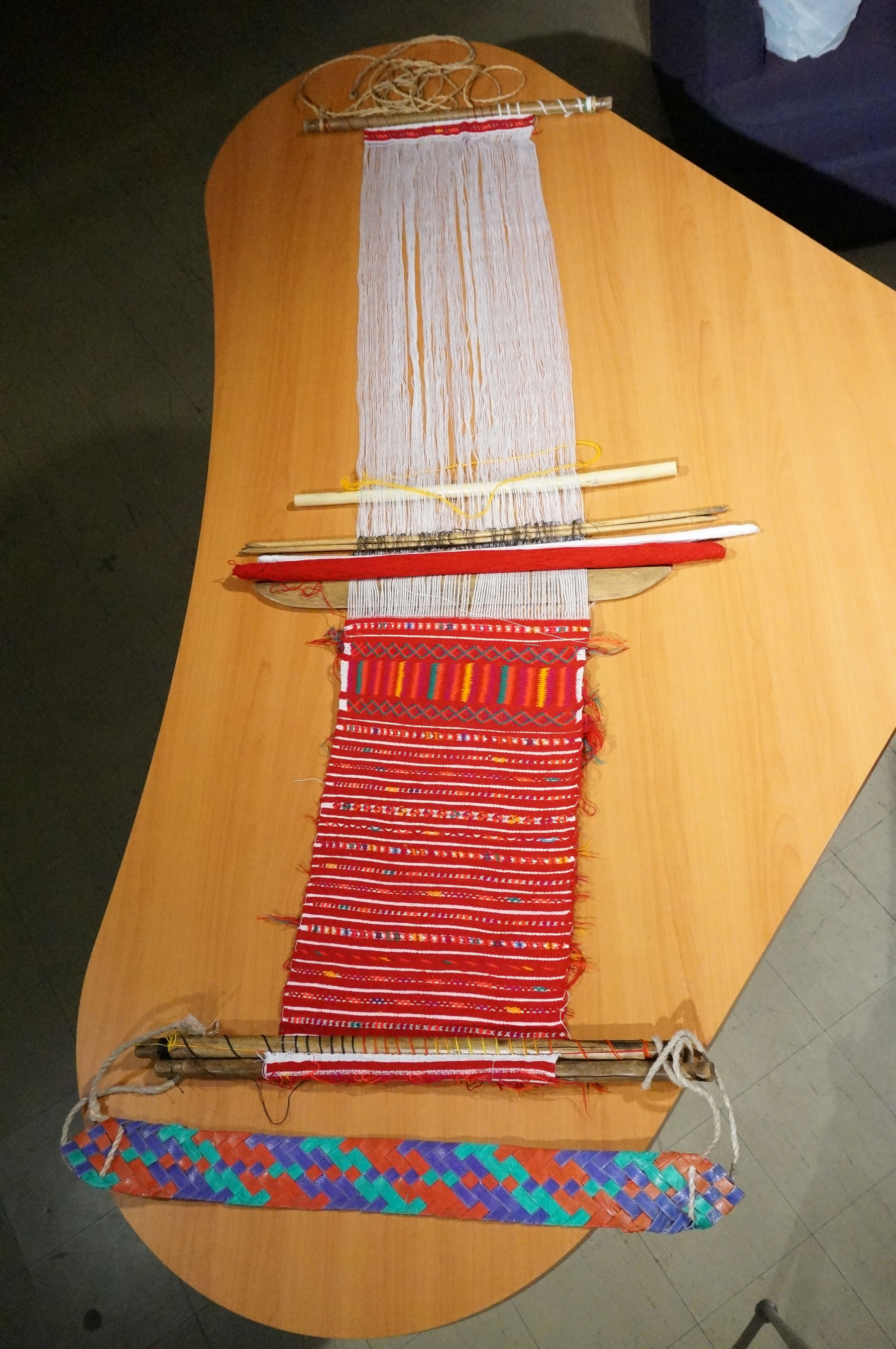A half finished red weaving on a backstrap loom.