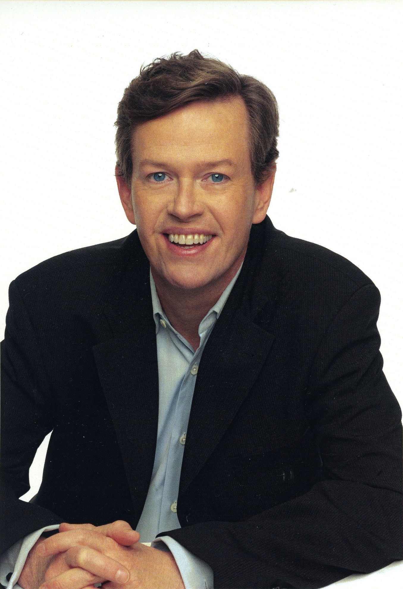 actor with dark hair smiles while wearing a white shirt and dark suit coat