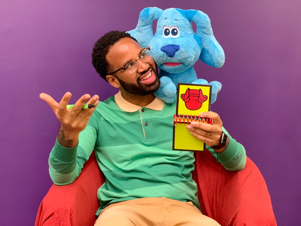 Brandon Lewis is dressed up like Steve from Blues Clues. A blue dog is peeping out from behind him.