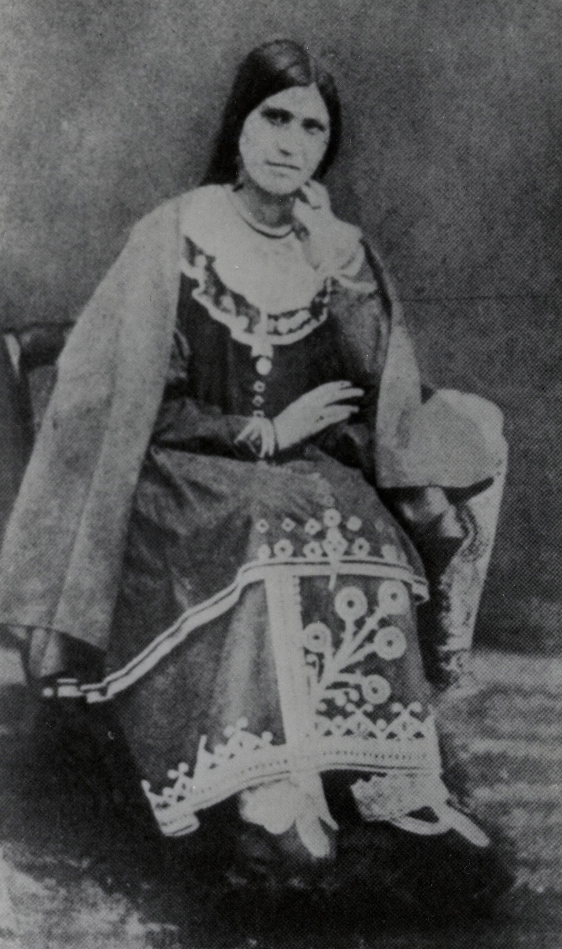 Caroline (Ga:hahno) Parker poses for a black and white photo, seated wearing a dress and cloak.