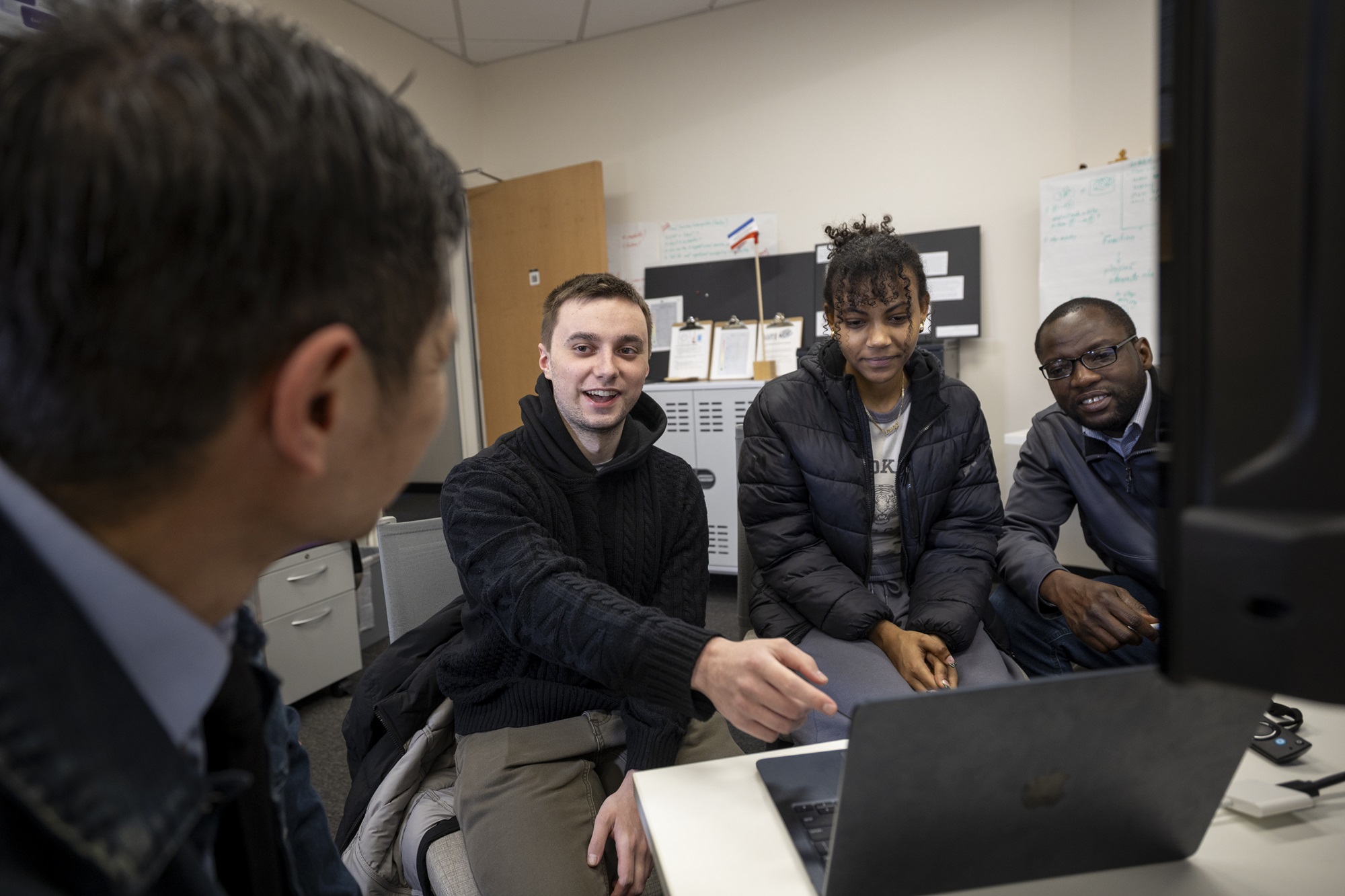 Three students sit around a laptop in the Cyber Cascade Risk lab at ETEC.