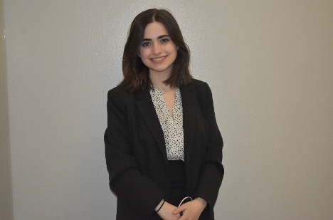 Student standing in front of white wall smiling.