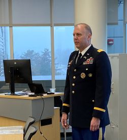 Col. Jeffrey Erickson stands in uniform near a window and a desk with a computer on it