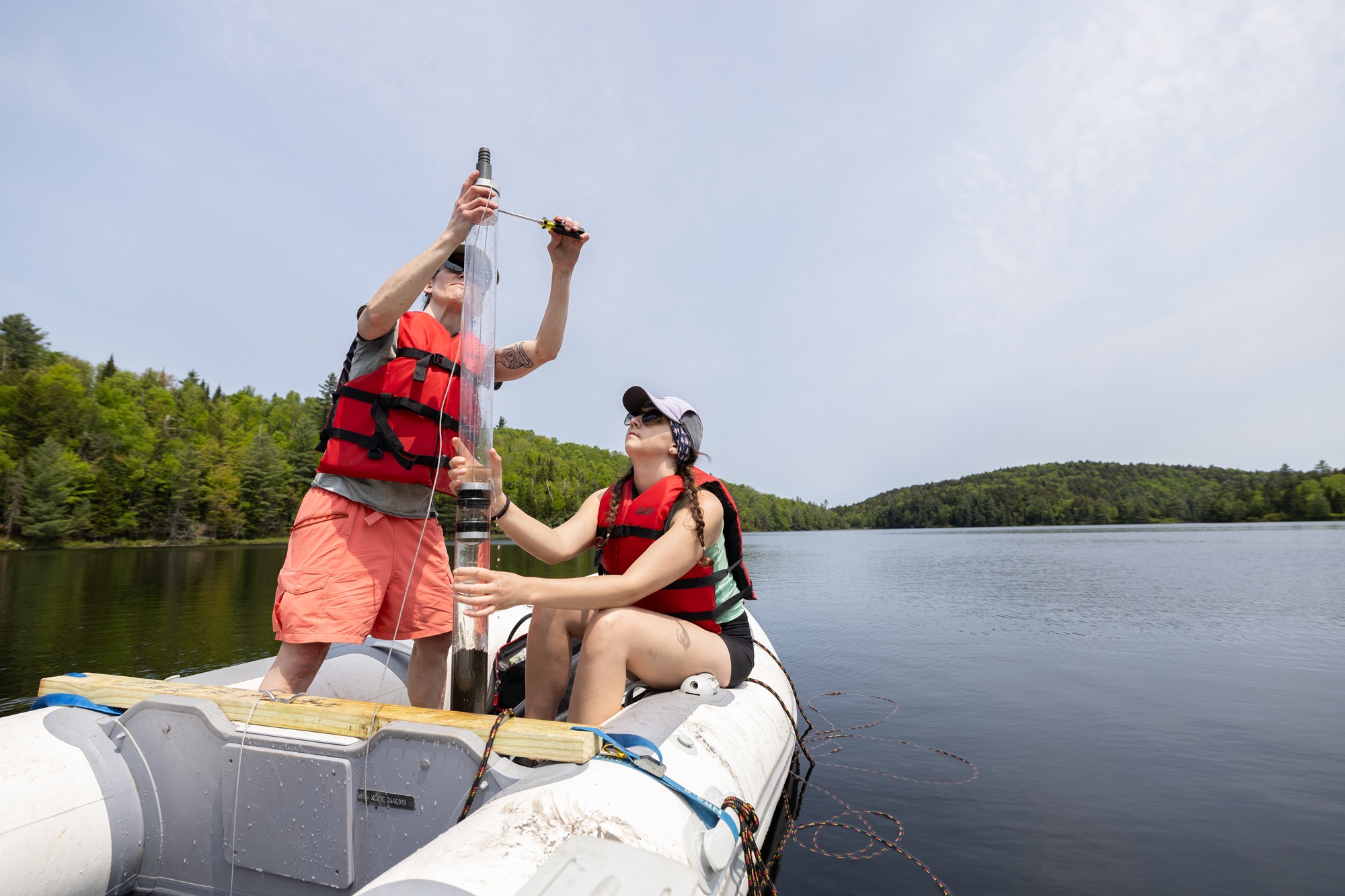Paleoclimate researcher Aubrey Hillman and graduate student Sumar Hart hold up a sediment core from a research boat on Black Pond.