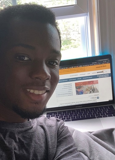 Amaechi Anyene takes a selfie in front of his laptop on the DHSES website homepage.