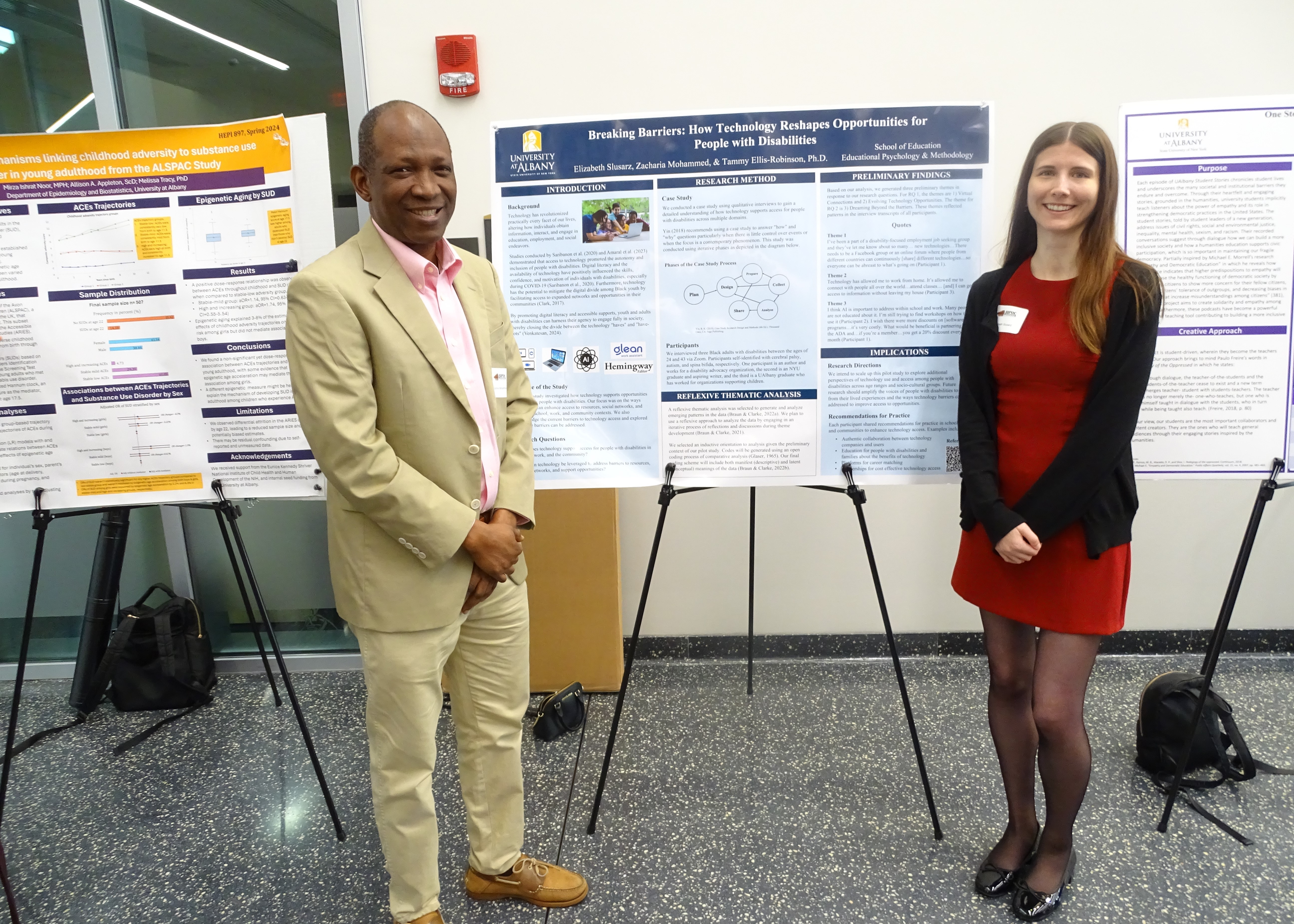 A man in a tan suit and a woman in a red dress with black cardigan smile in front of their poster titled "Breaking Barriers: How Technology Reshapes Opportunities for People with Disabilities."