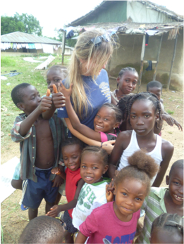 A Peace Corp volunteer is surrounded by children giving her a hug.
