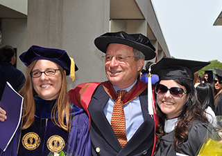 Stuart Swiny in regalia hugs two UAlbany students at commencement