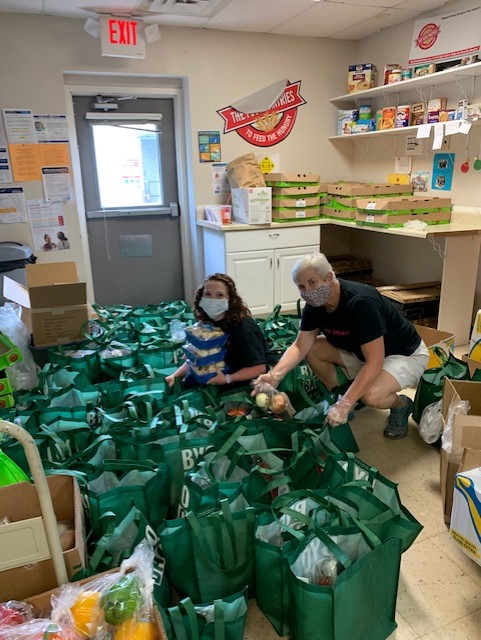 Elizabeth and a coworker bag healthy produce for community members into green bags. 