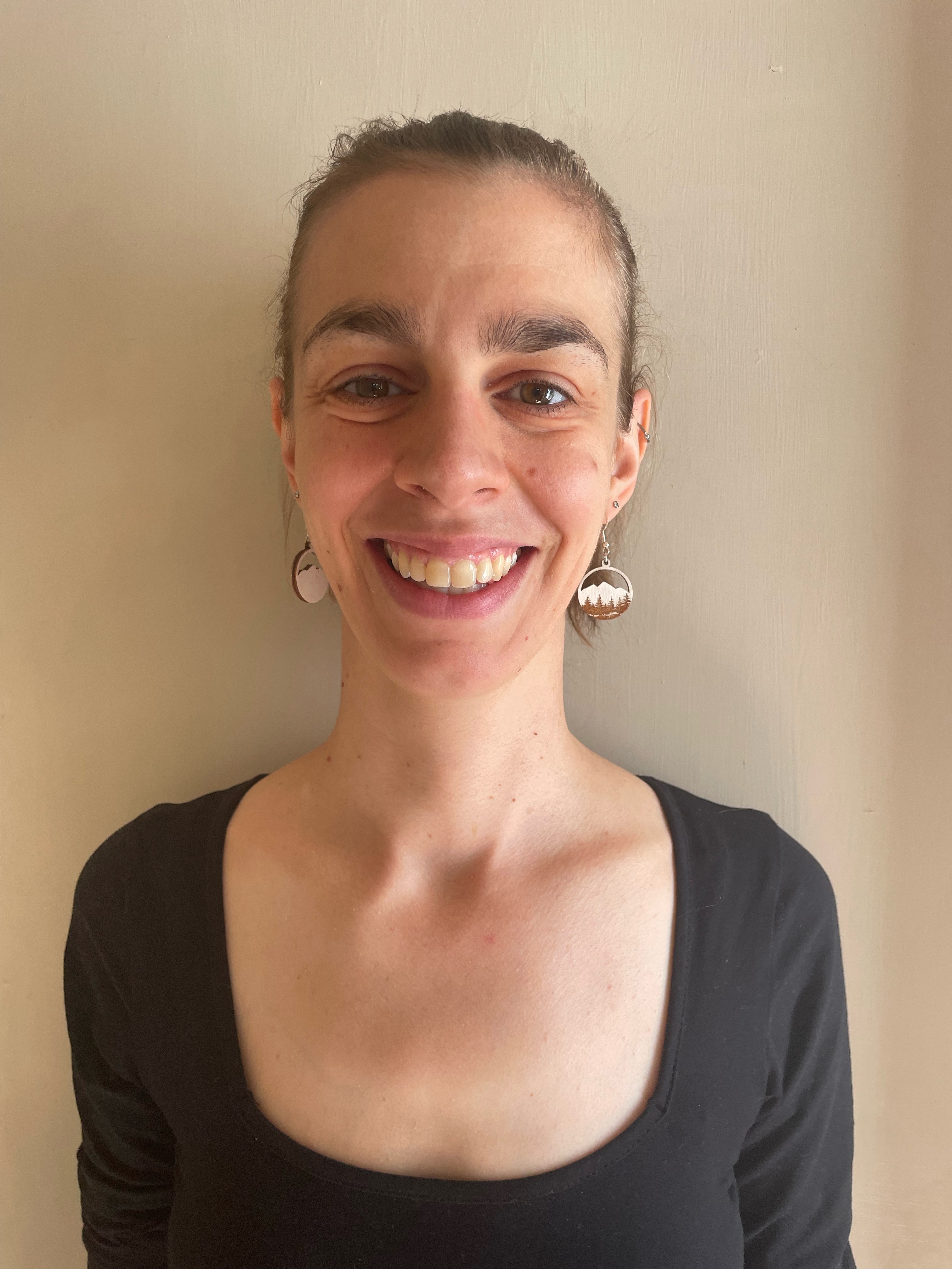 A young woman wearing a black top smiles for a portrait against a beige wall. 