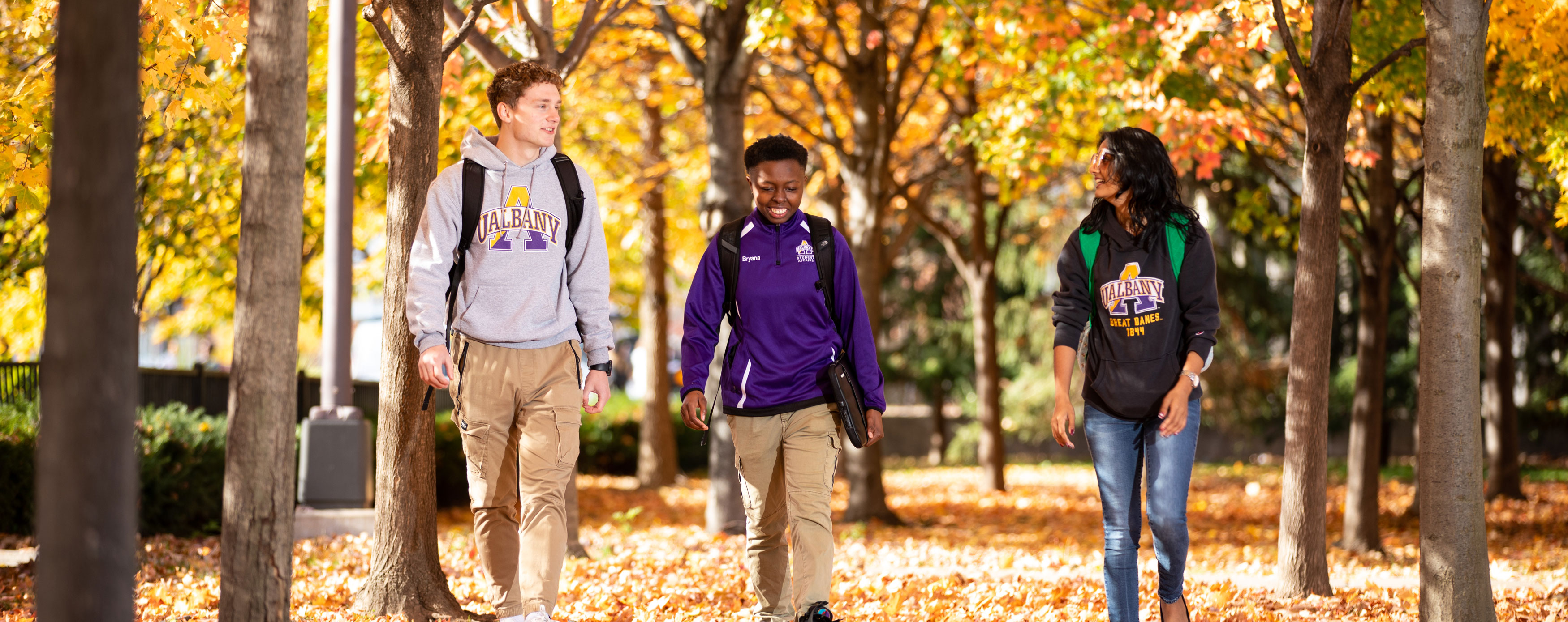 Three students smile as they walk through fall foliage on campus.