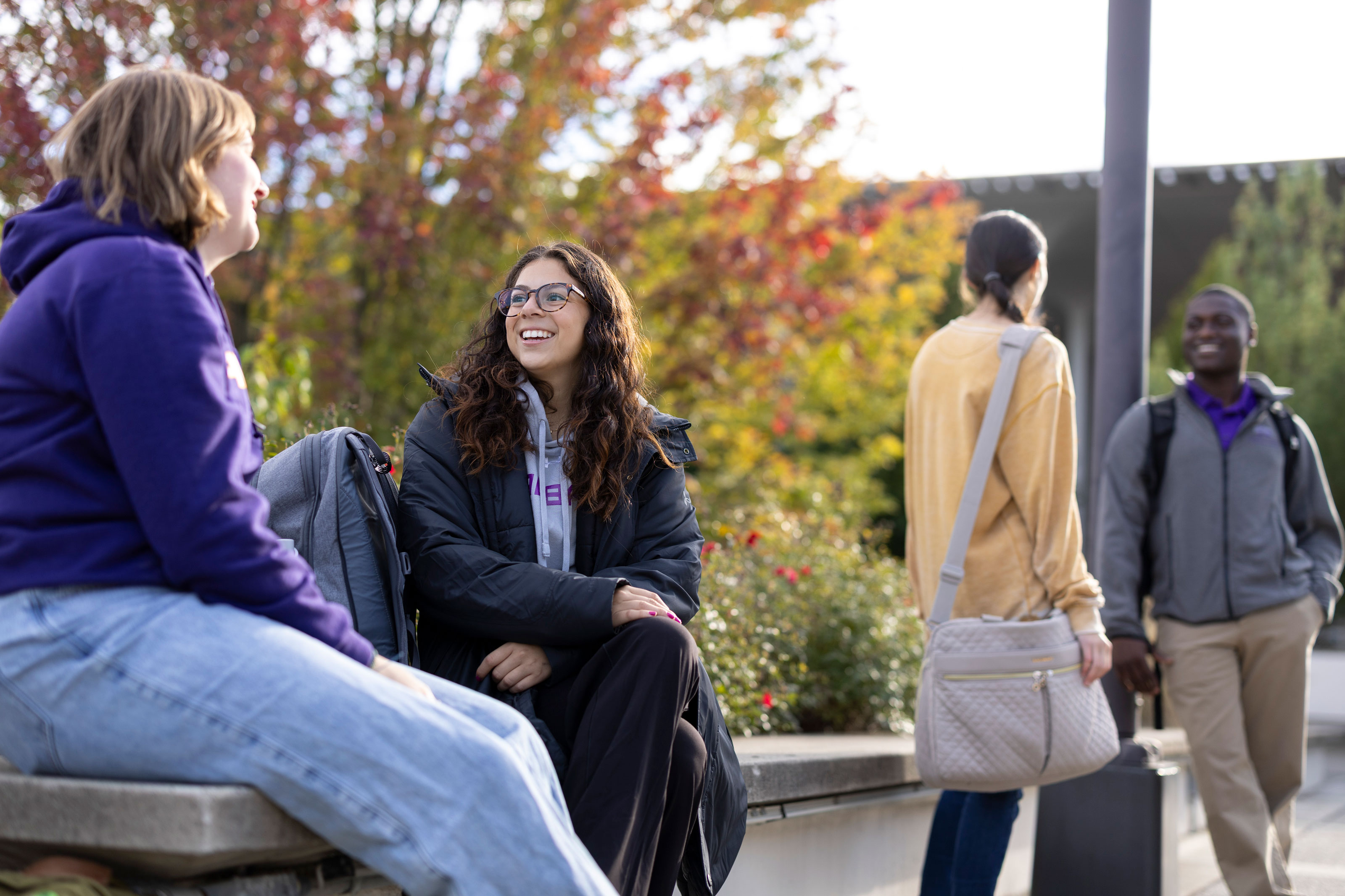 Two students sit on a bench and smile as they talk, while two other students stand nearby conversing.