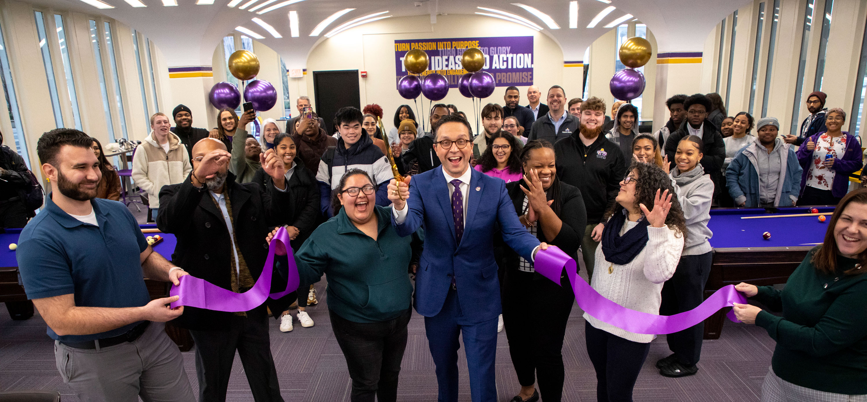 Student Affairs leadership cheers and smiles as they cut a purple ribbon inside UAlbany's new game room.