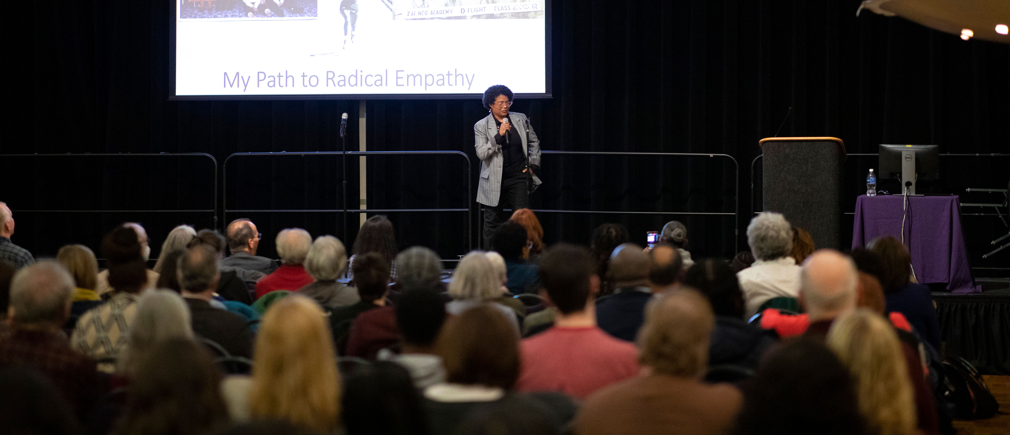 Terri Givens stands on stage before a presentation slide that says "My path to radical empathy," and speaks to her a seated audience using a microphone.
