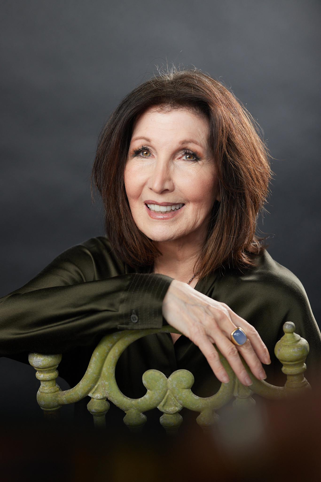 woman with dark hair smiles as arm is draped over the back of a chair