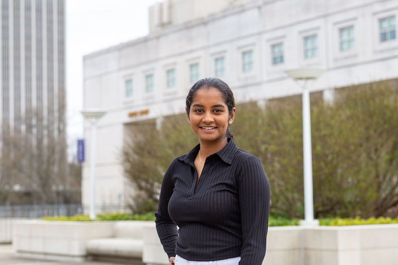 A young woman in a black shirt poses for a portrait outside.