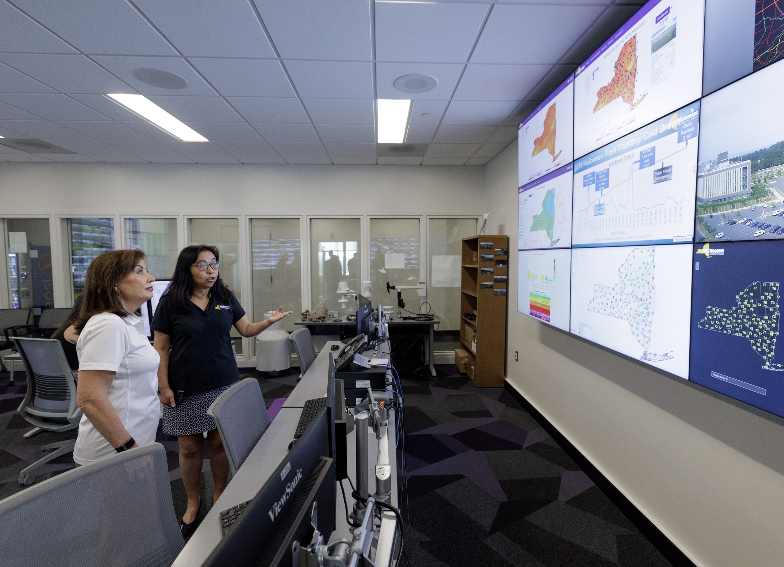 June Wang points at weather maps with Governor Kathy Hochul inside the New York State Mesonet operations center.