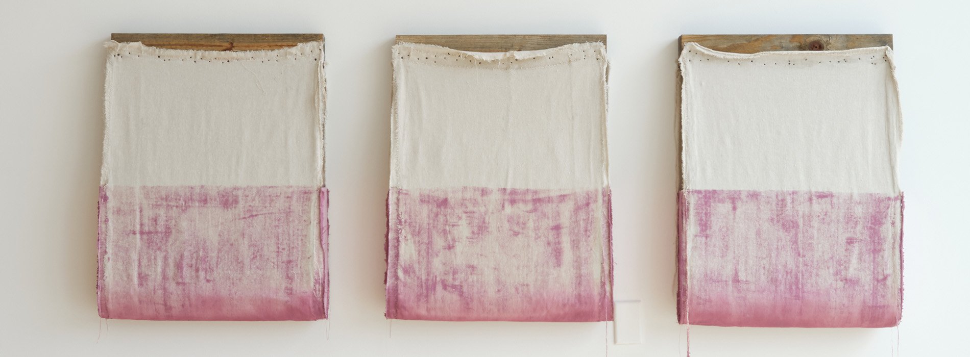 Three woosen frames hang on the wall, white and pink fabric draping off of them.