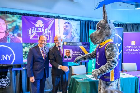 Two laughing men accept an oversized ID card from a mascot of a Great Dane.