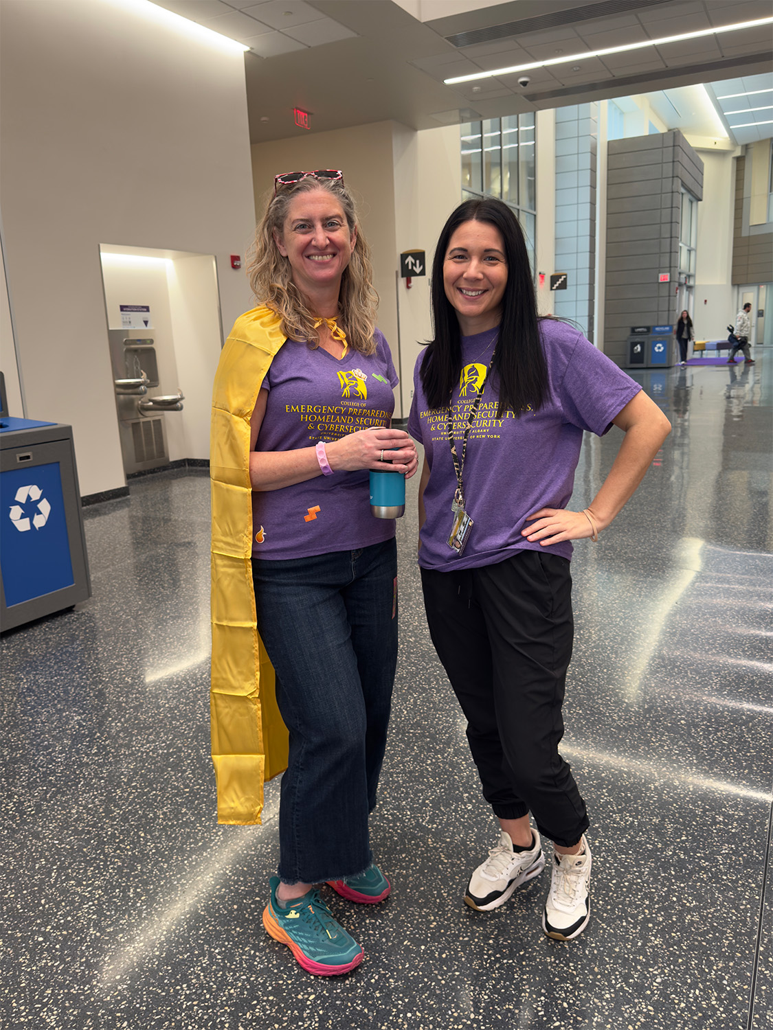 Jen Goodall stands with a super hero cape on next to Erin Couture at the ETEC atrium.
