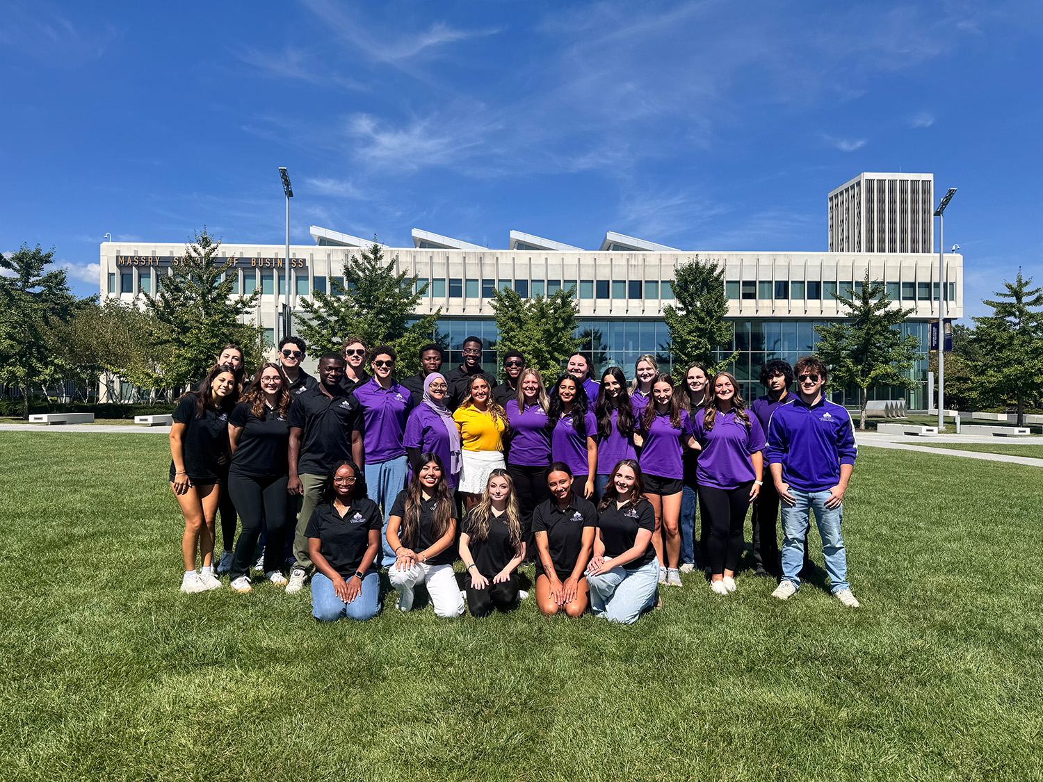 A group of students and staff members posed in front of the Massry School of Business.