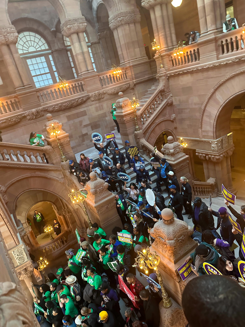 Over 70 students and supporters attended LEAD 2024. Here, LEAD participants pour down a stairwell in the NYS Capitol during the April rally centering child welfare legislation. The walls are a tan stone and accent lights shine yellow.