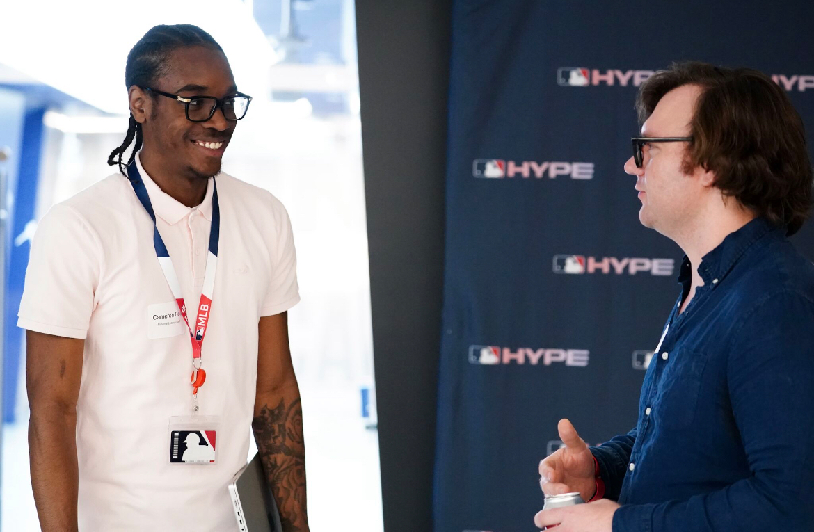 Cameron Felix wears a white polo and MLB tag, while meeting with his appointed mentor Andrew Ogg, an MLB tech services engineer.