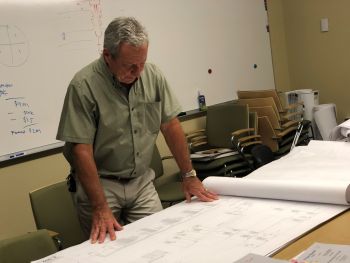 Michael Vadney, standing, looks over architectural plans in a room with a white board behind him