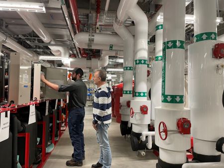 Two men in a mechanical room look into a control box